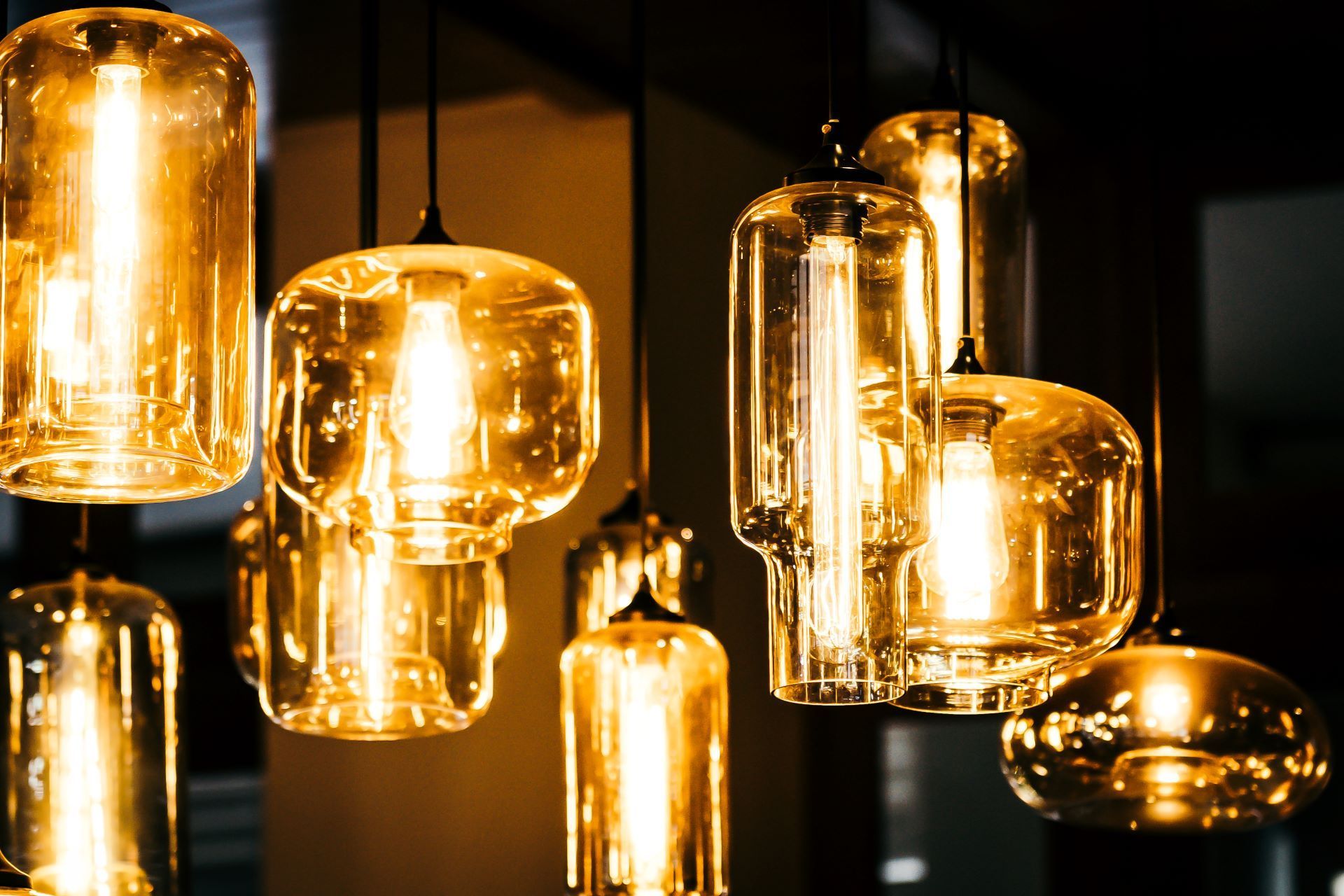 A cluster of glowing, amber-toned glass pendant lights with warm Edison-style bulbs suspended in a dimly lit space.