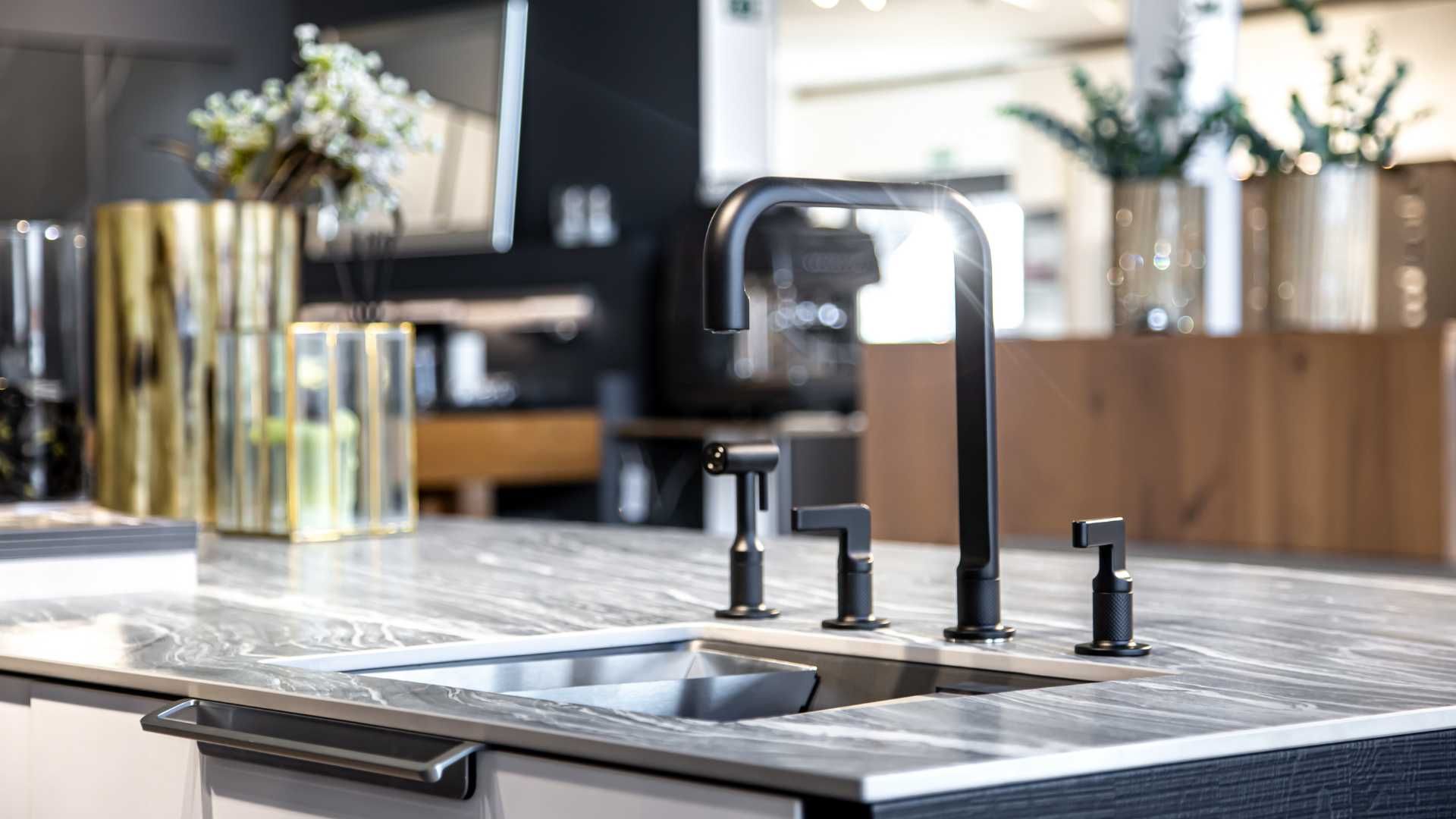A kitchen sink with a black faucet on a granite counter top.