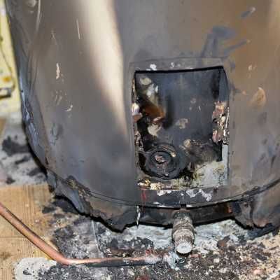 A water heater that has been damaged by fire is sitting on the floor.