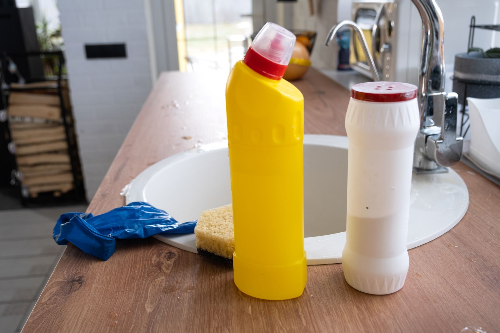 Cleaning supplies on a kitchen counter by a sink, including a yellow spray bottle and white bottle.