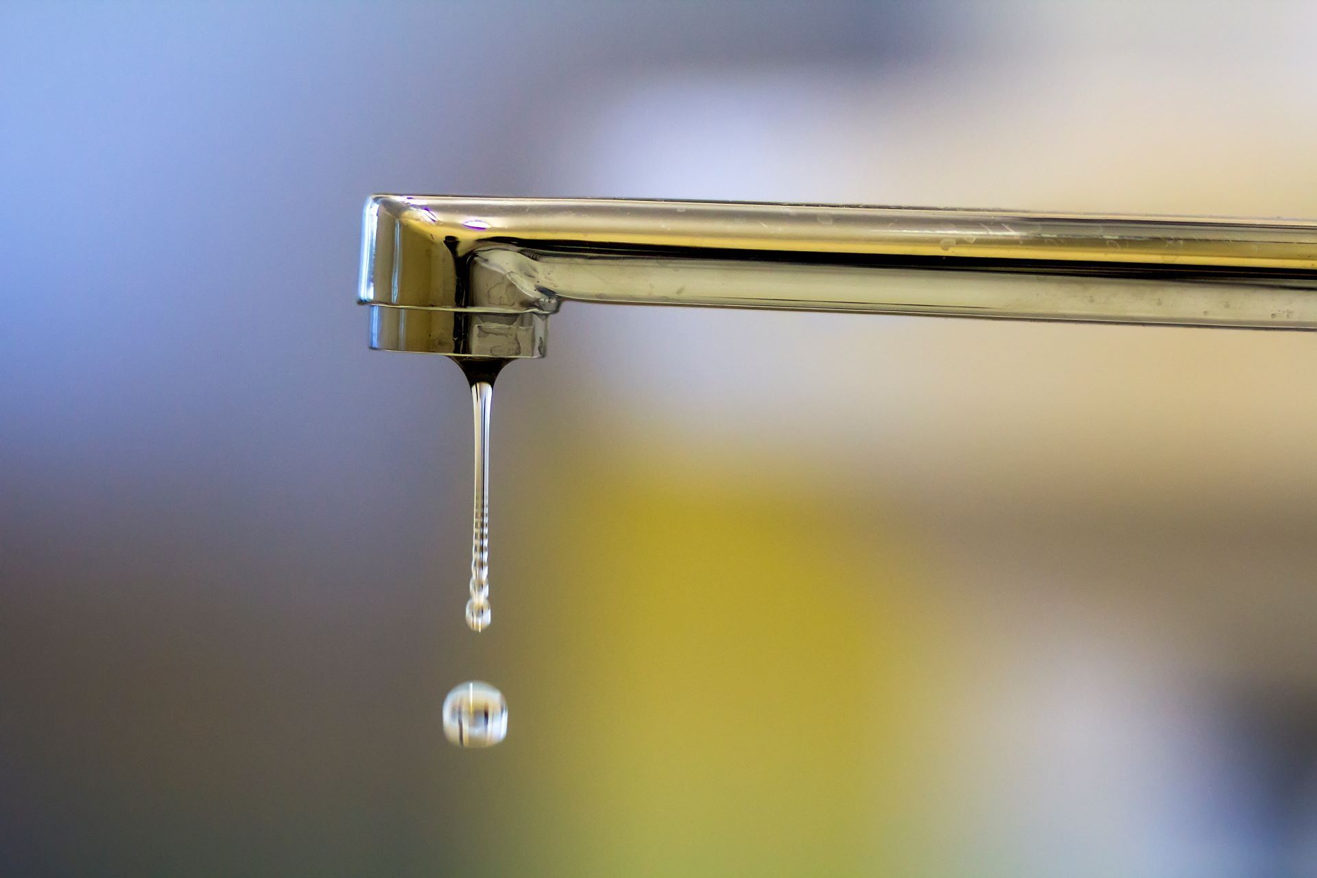 A chrome faucet with a single water droplet falling.