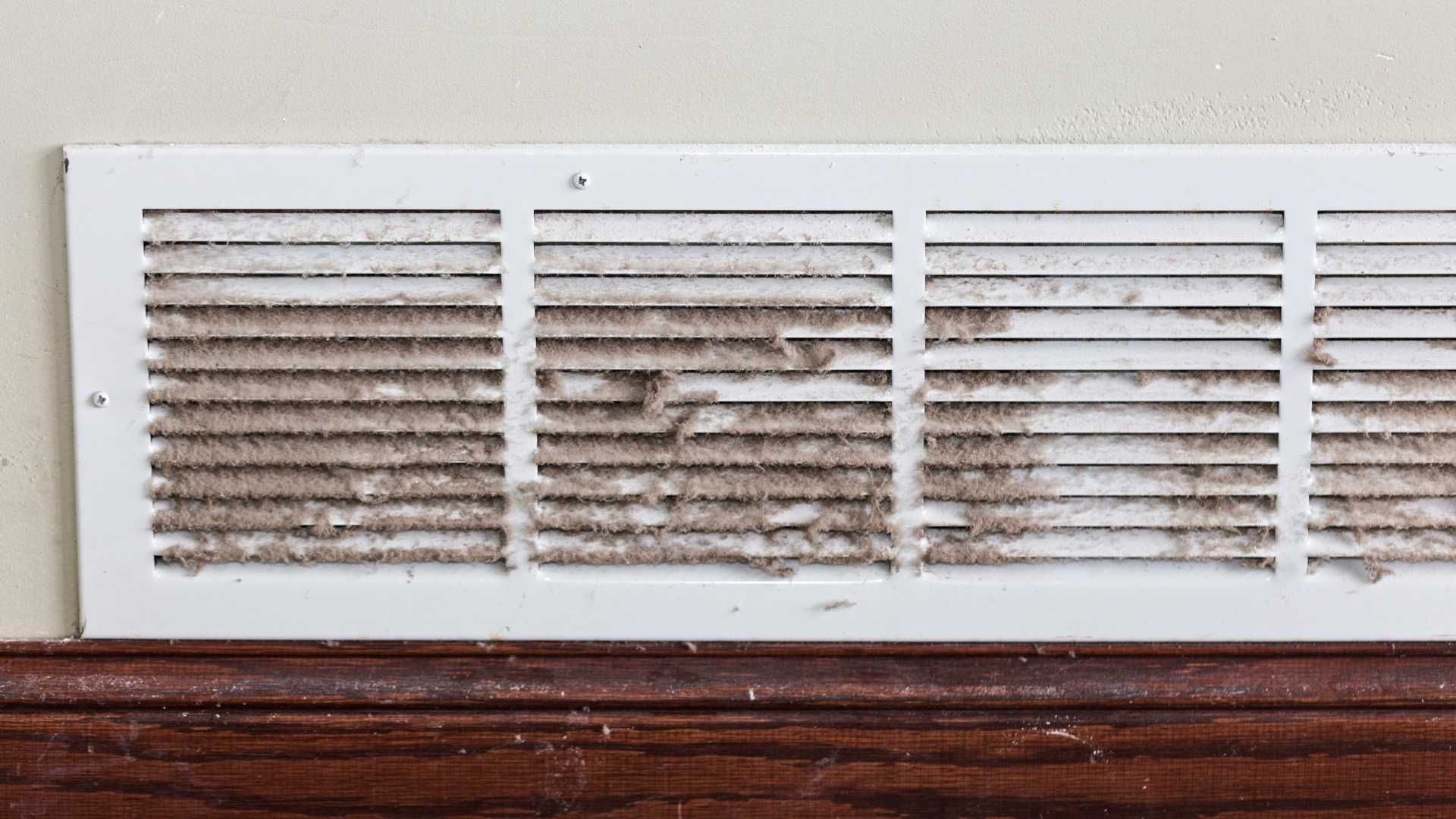 A dirty air vent is sitting on top of a wooden shelf.