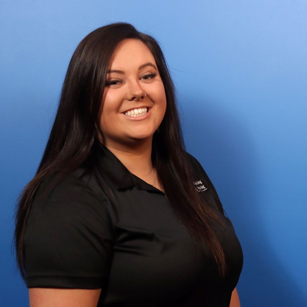 A woman in a black shirt is smiling in front of a blue background