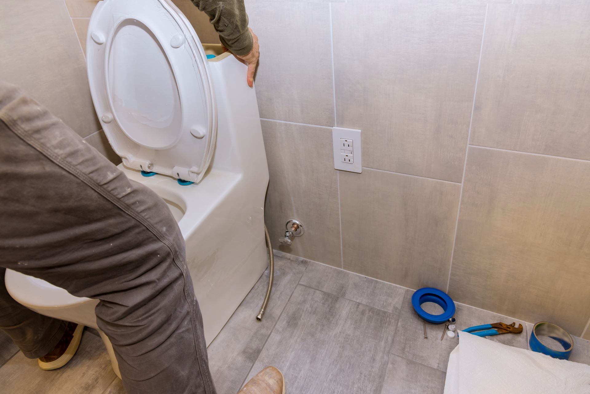 Person installing a white toilet in a bathroom with gray tile.