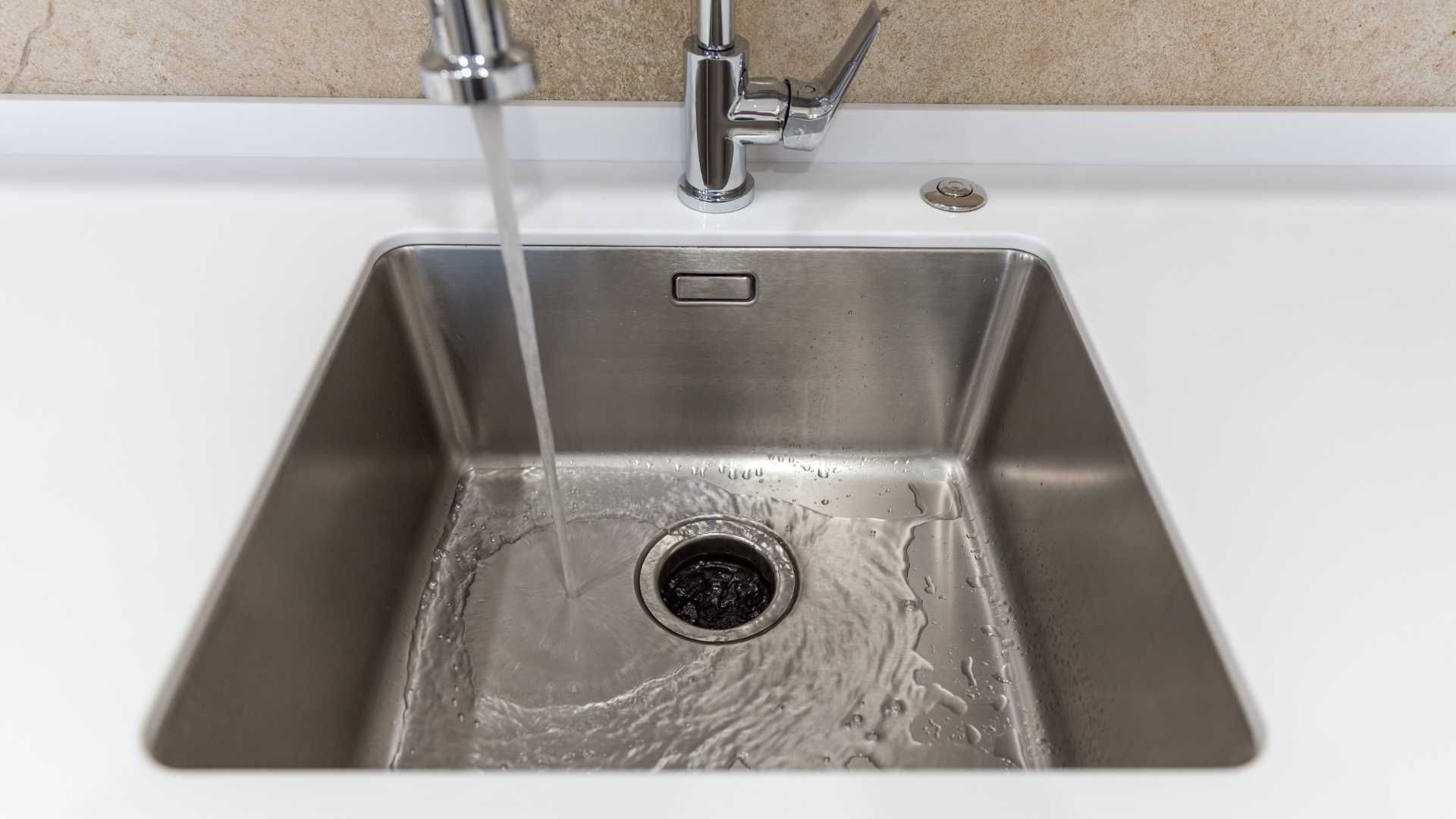 A stainless steel kitchen sink with water running from the faucet.