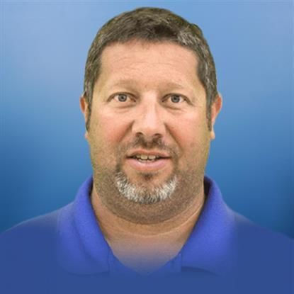 A man with a beard is wearing a blue shirt and smiling.