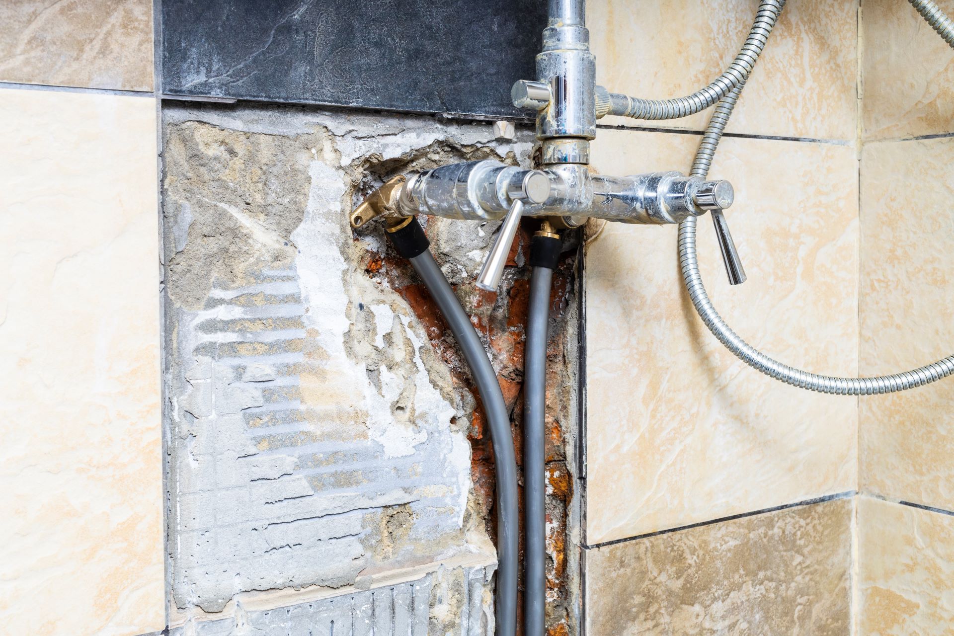 Exposed plumbing in a tiled shower wall with pipes, fixtures, and damage.
