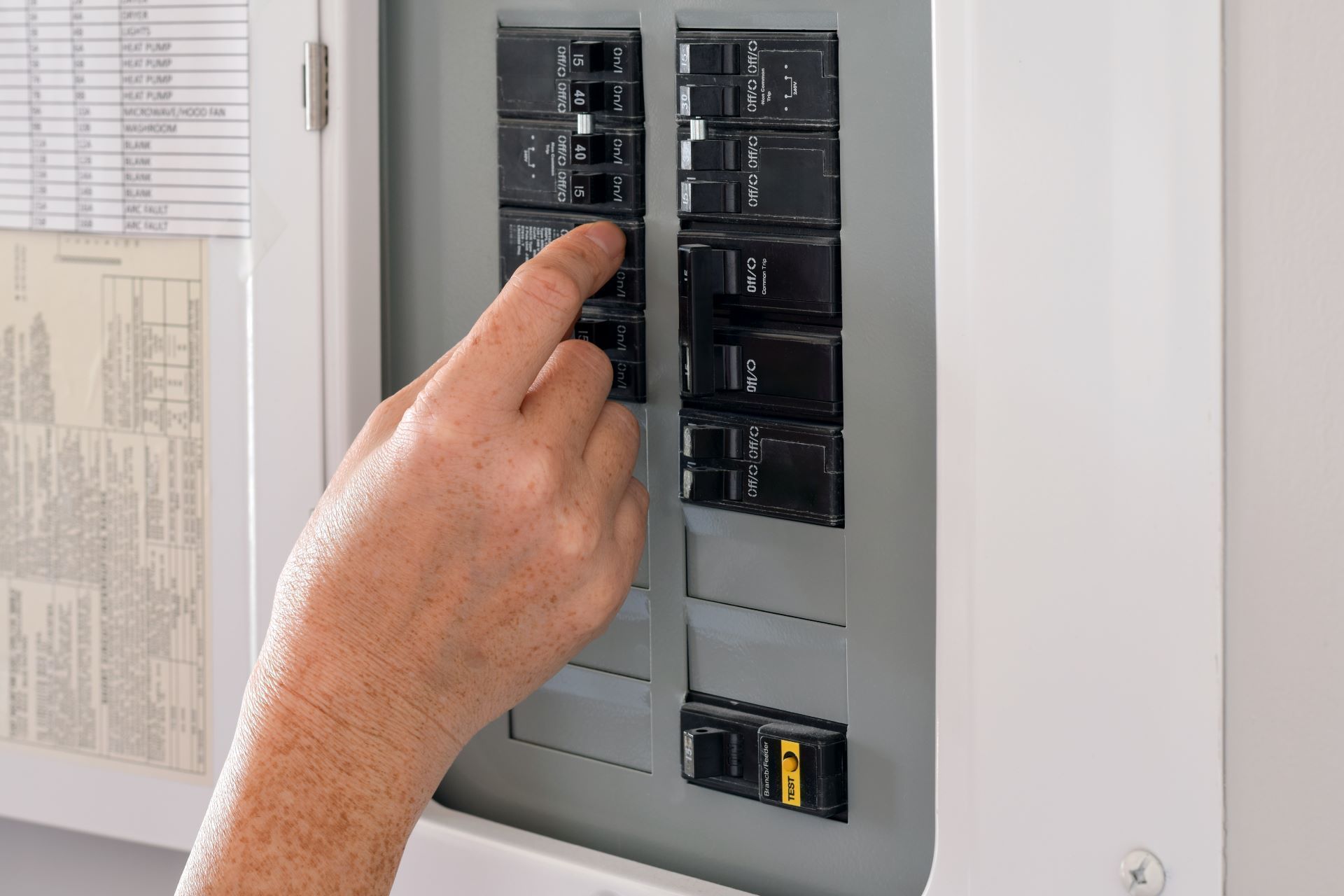 A hand flips a circuit breaker switch inside an electrical service panel.
