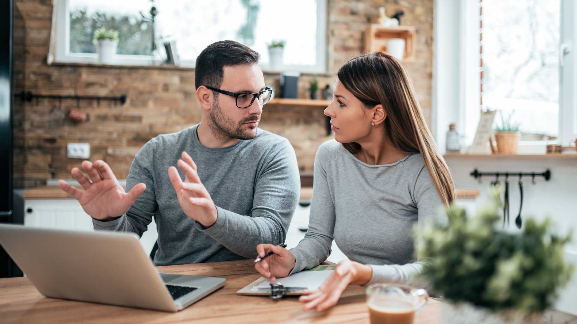 A man and a woman are sitting at a table looking at a laptop computer.
