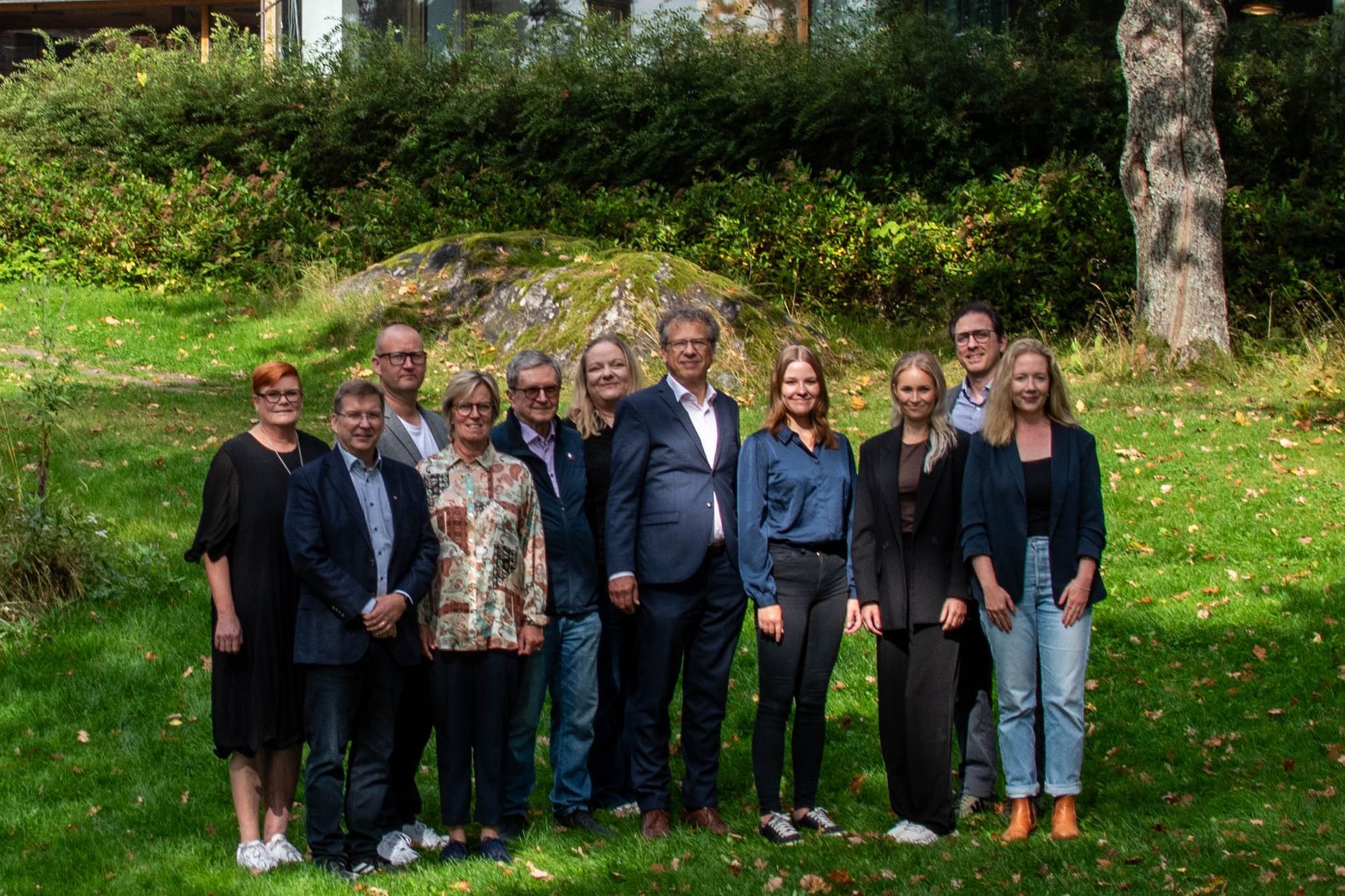 A group of eleven professionals stands in a grassy park setting, posing for a photo outdoors.