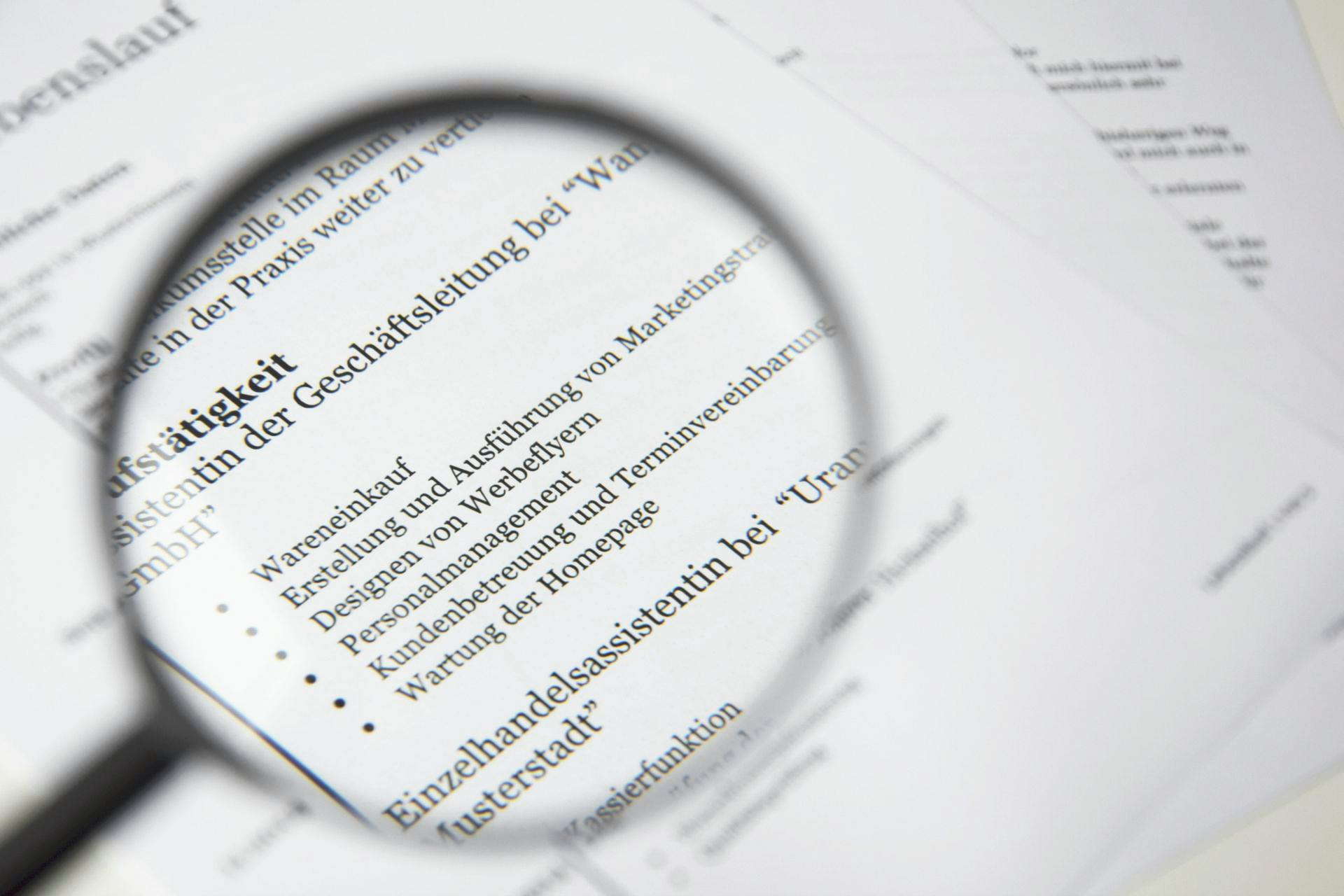 A magnifying glass focused on a resume written in German, highlighting a work experience section with bullet points.