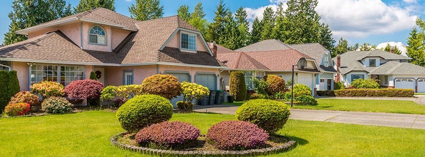 Houses with well-manicured lawns and landscaping. Sunny day with trees and blue sky.