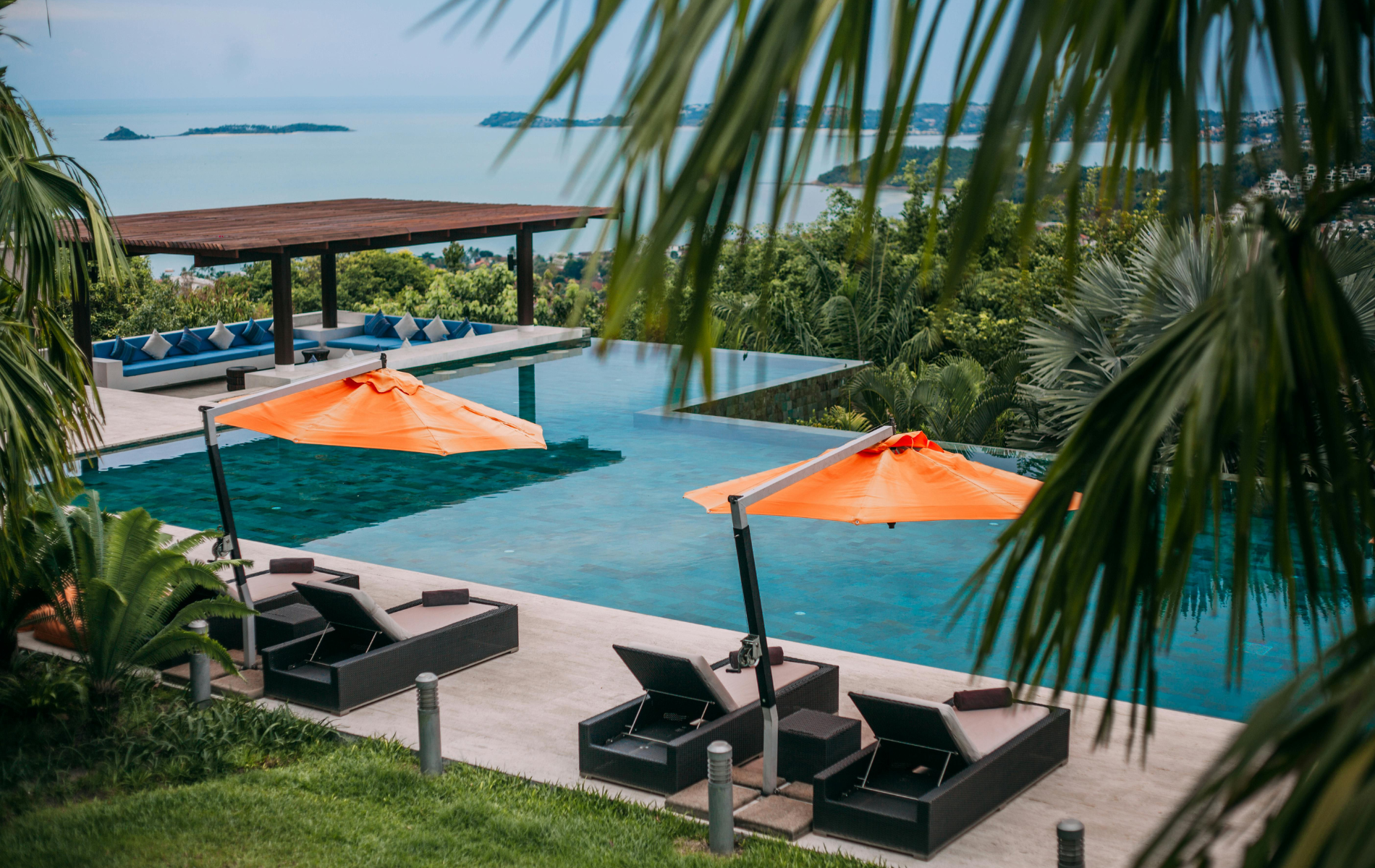 Luxury pool overlooking ocean, with orange umbrellas, lounge chairs, and tropical foliage.