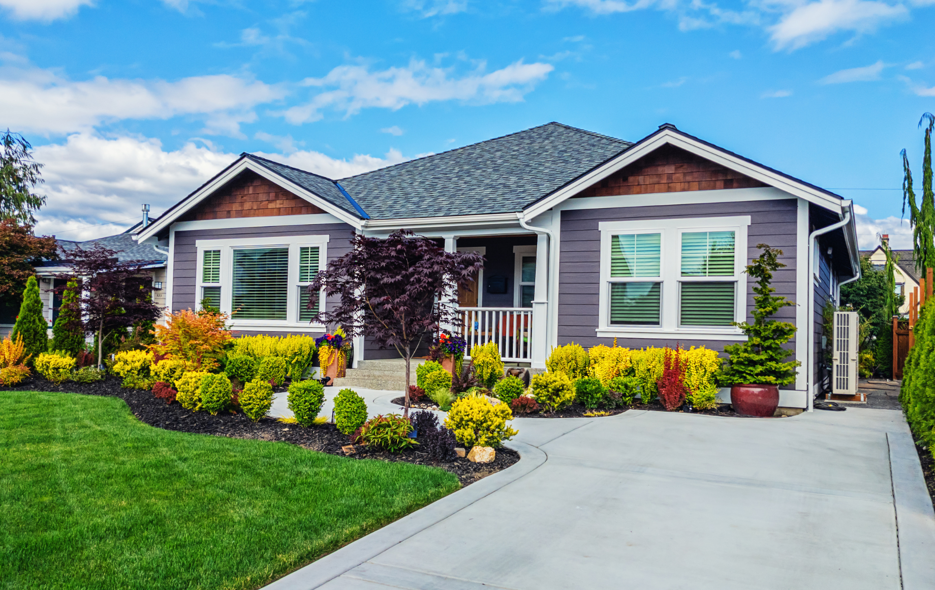 Gray house with landscaped yard and a curved driveway on a sunny day.