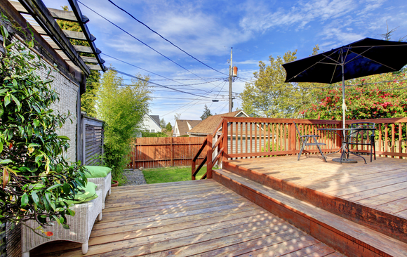 Wooden backyard deck with umbrella and red fence under a blue sky.