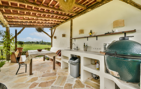 Outdoor kitchen with green grill, sink, table, and open sky view.