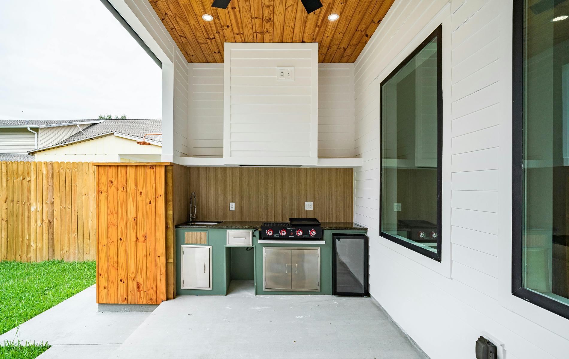 Outdoor kitchen with a grill, cabinets, and a wine cooler on a patio.