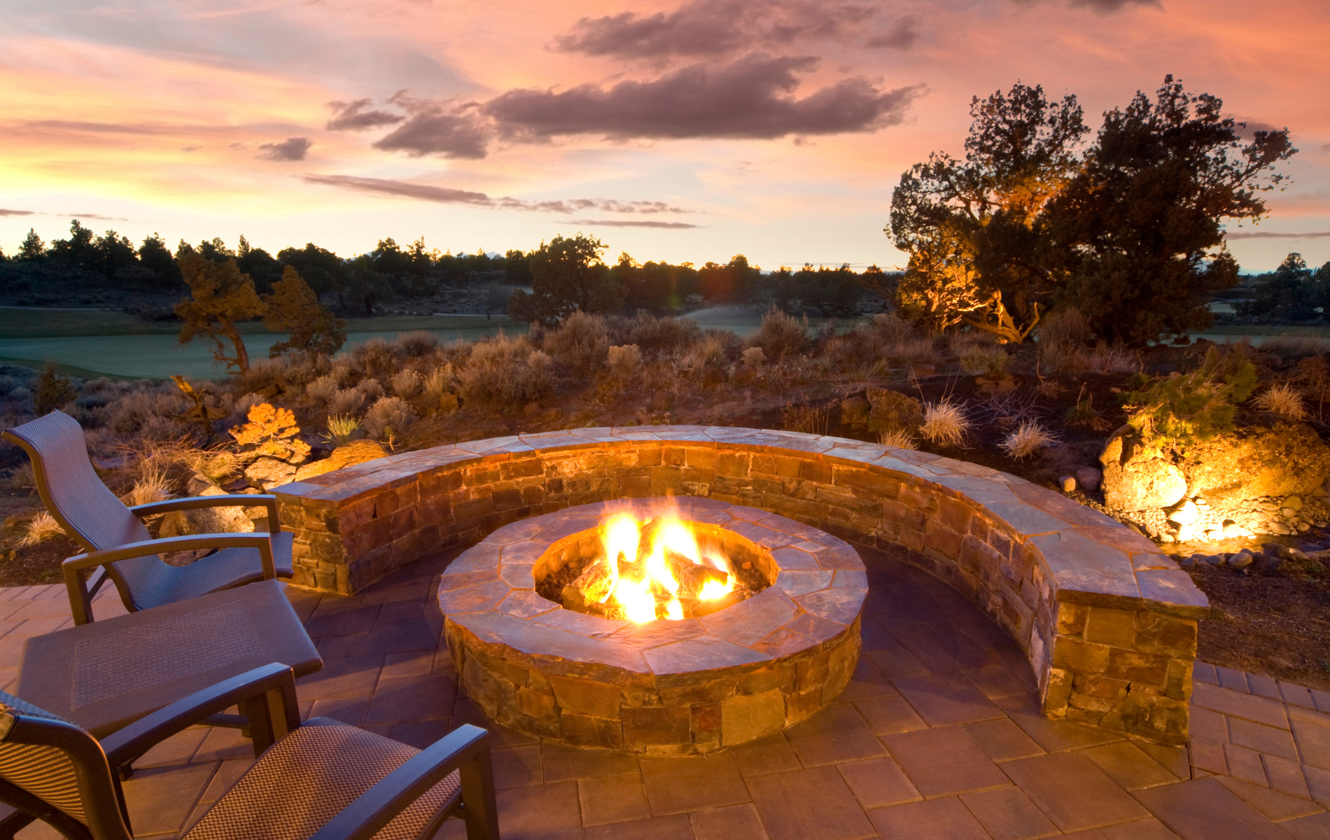 Fire pit with curved stone seating at sunset, surrounded by landscaping.
