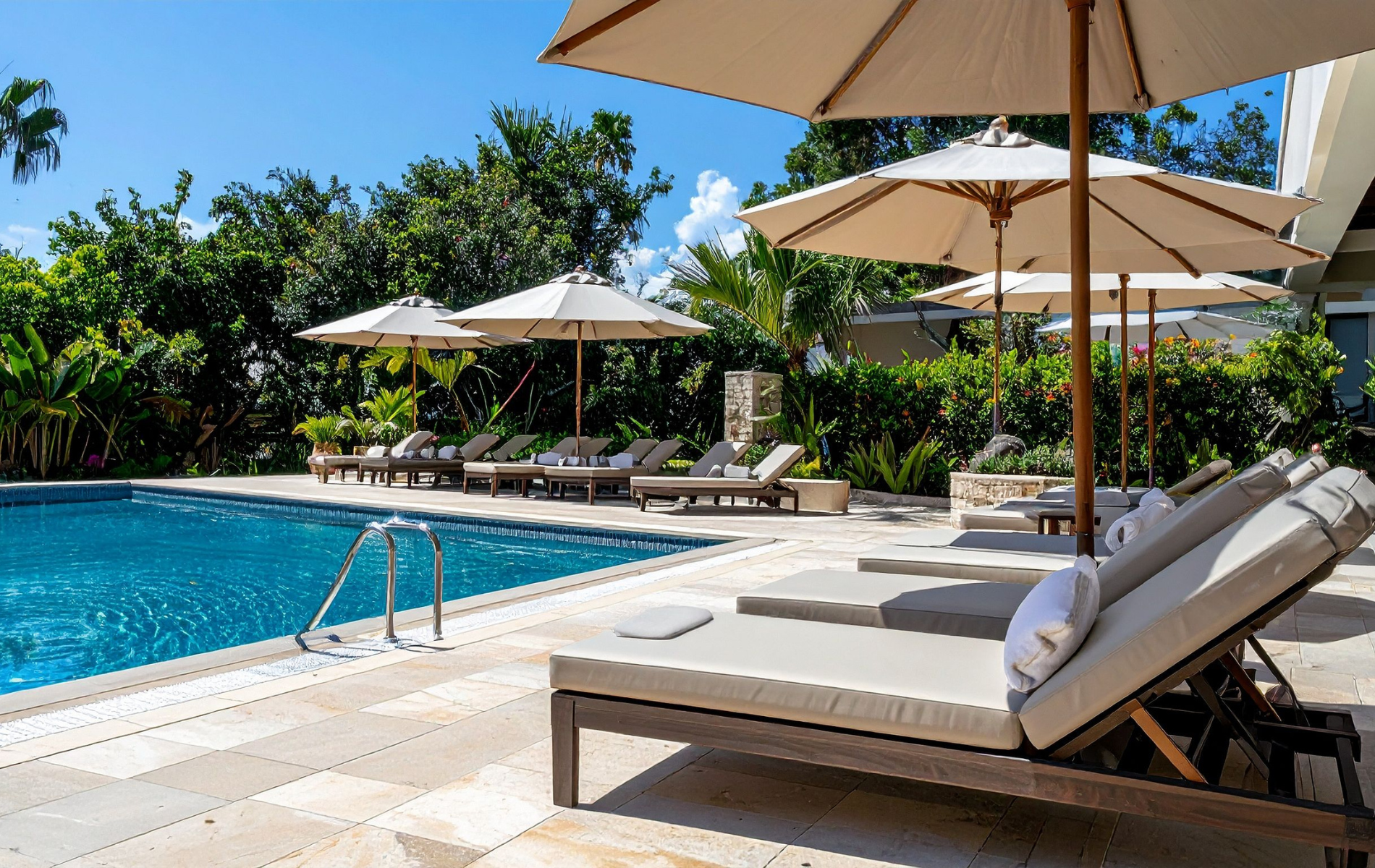 Poolside scene: lounge chairs, umbrellas, and clear blue water under a sunny sky.