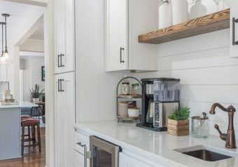 White kitchen with coffee maker, floating shelf, and copper faucet.