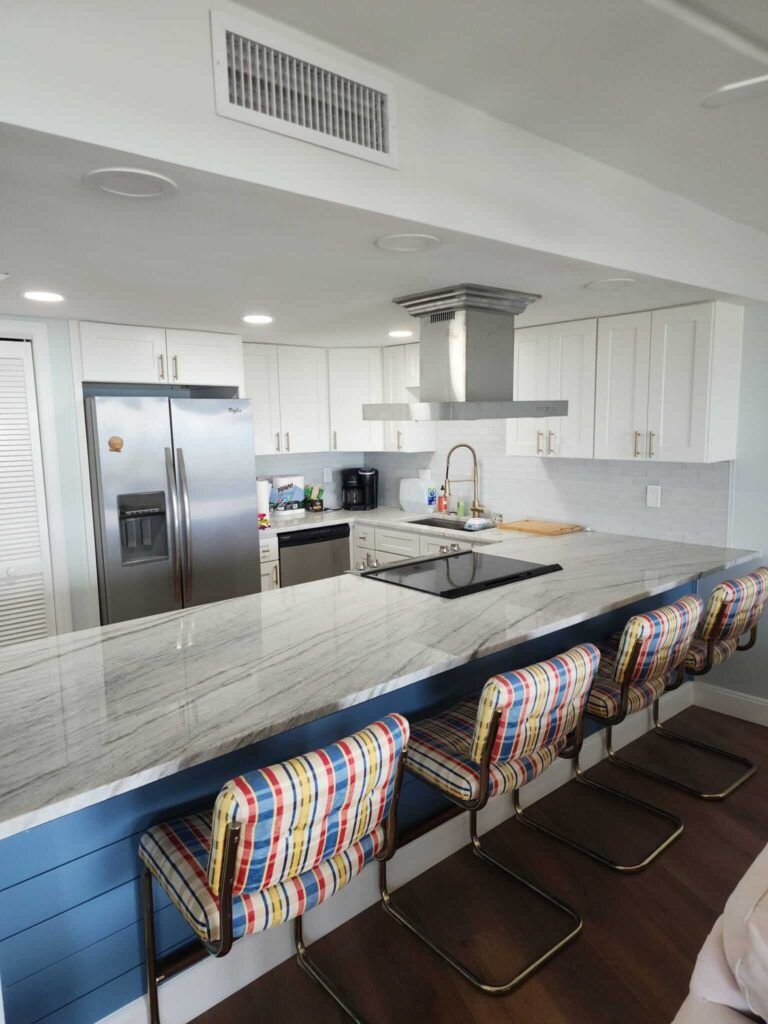 Modern kitchen with white cabinets, stainless steel appliances, and a large island with colorful stools.