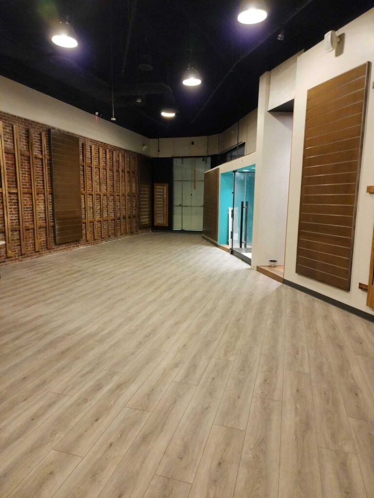 Empty room with wood-look flooring, dark ceiling, and wood-paneled walls. A glass-door space is in the back.