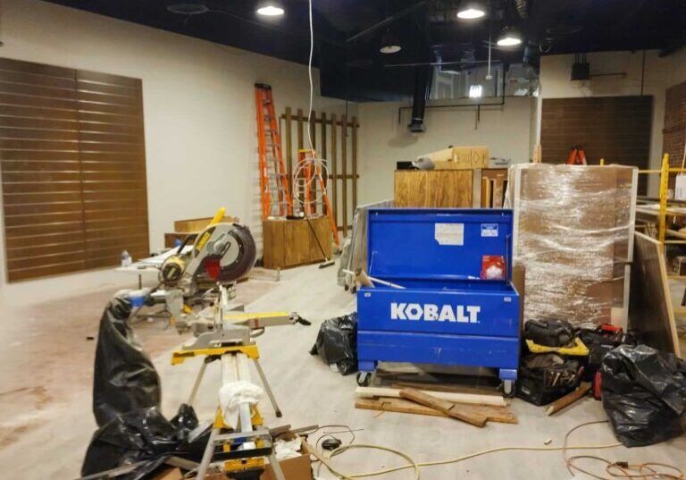 Construction site interior: a circular saw, tool chest, wood panels, and a ladder.