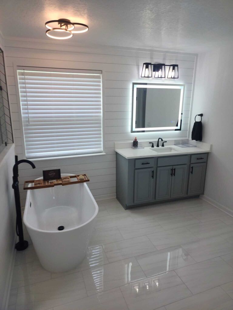 Modern bathroom with a tub, vanity, and large mirror. White and gray tones dominate the space.