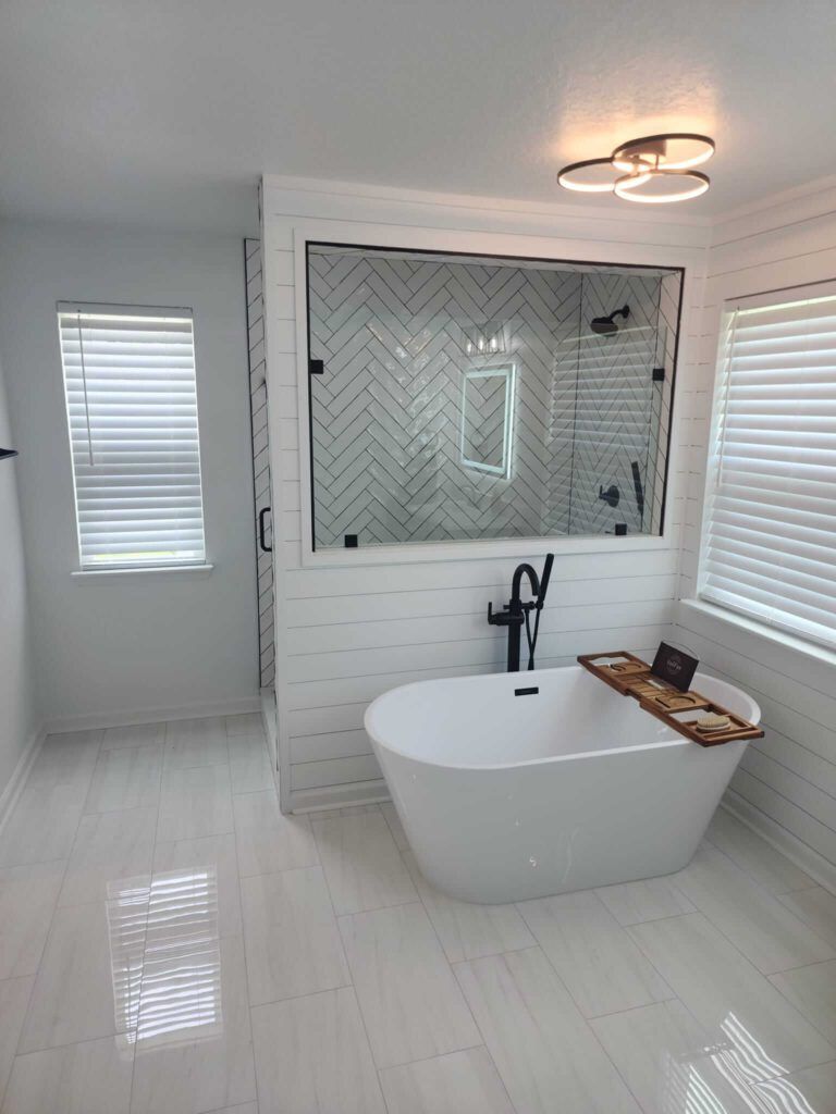 Modern white bathroom with freestanding tub, glass shower, and black fixtures.