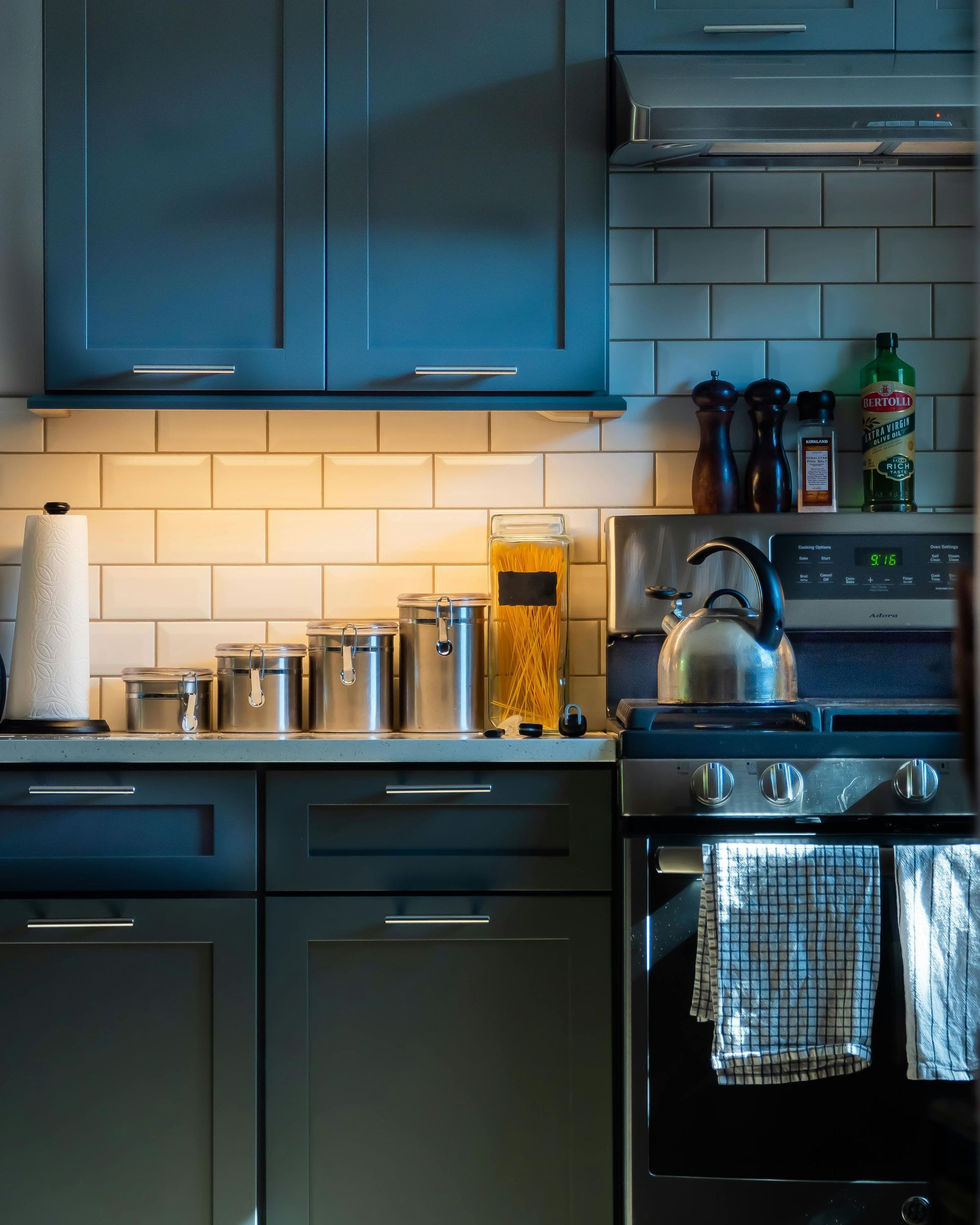 Kitchen with blue cabinets, white subway tile, stainless steel appliances, and various canisters and jars.