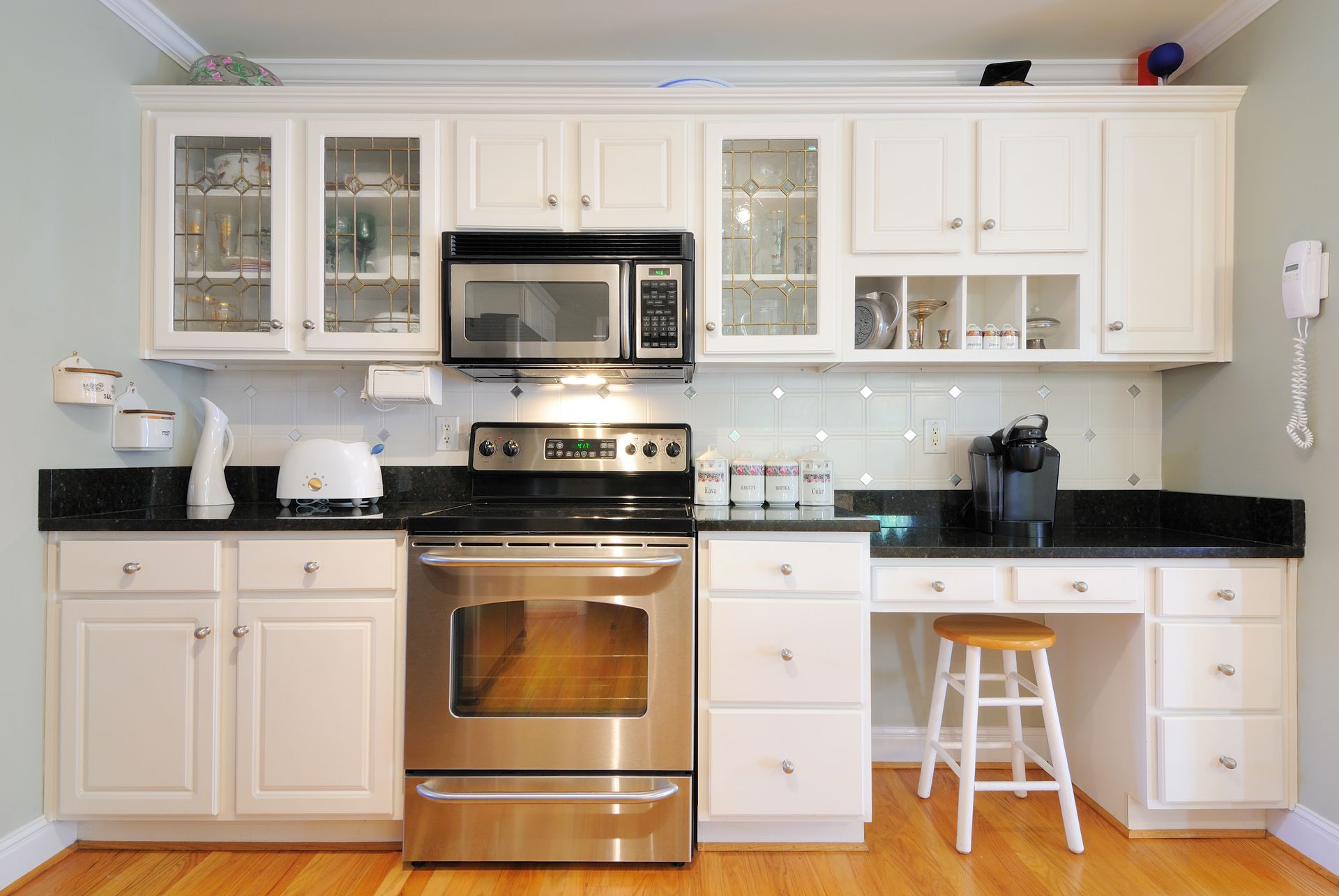 White kitchen with stainless steel appliances, black countertops, and wooden floor.