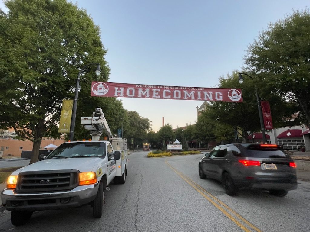 Two cars are driving under a banner that says homecoming
