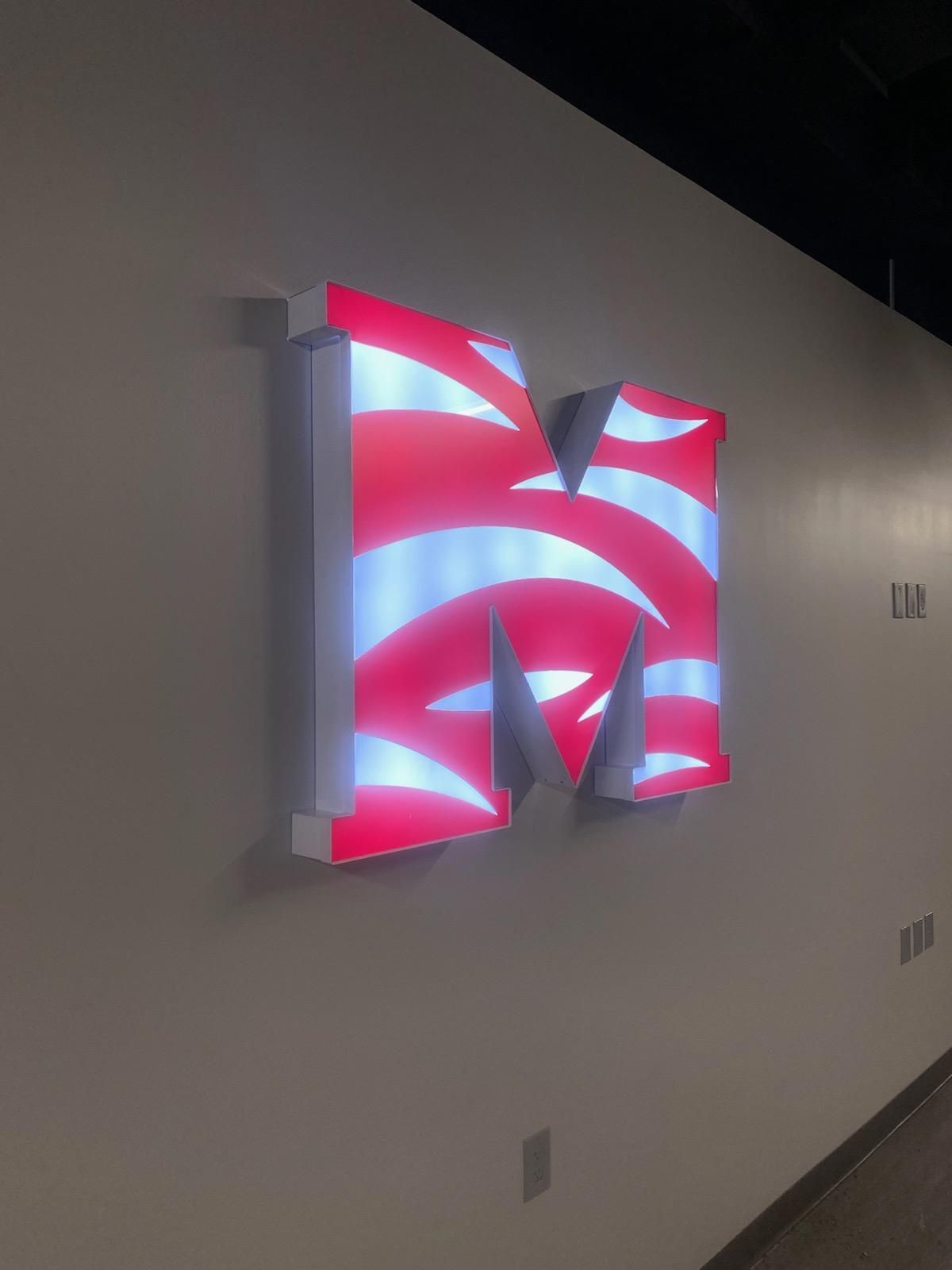 A red white and blue letter m is lit up on a wall