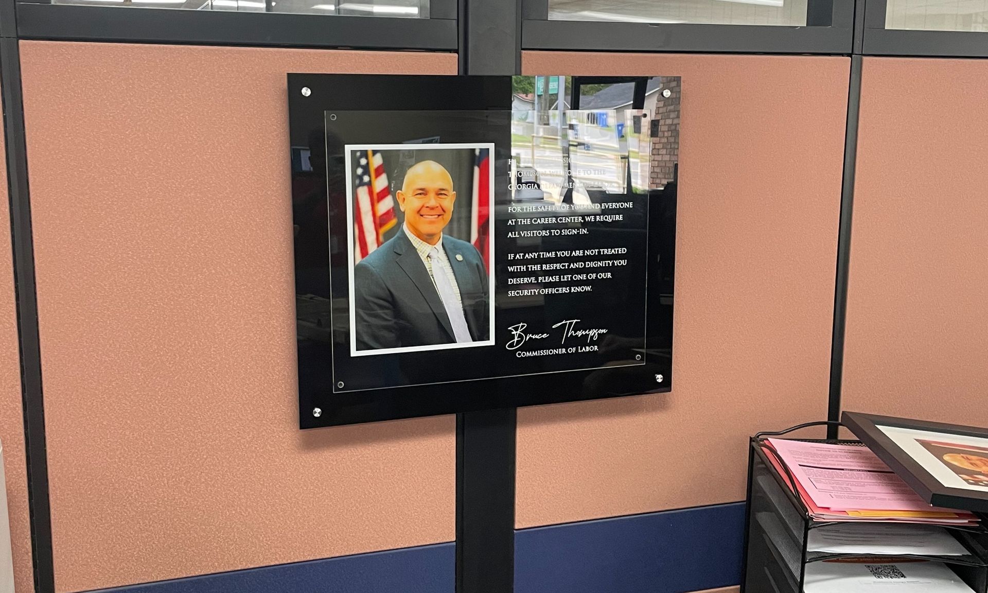 A picture of a man is hanging on a wall in a cubicle