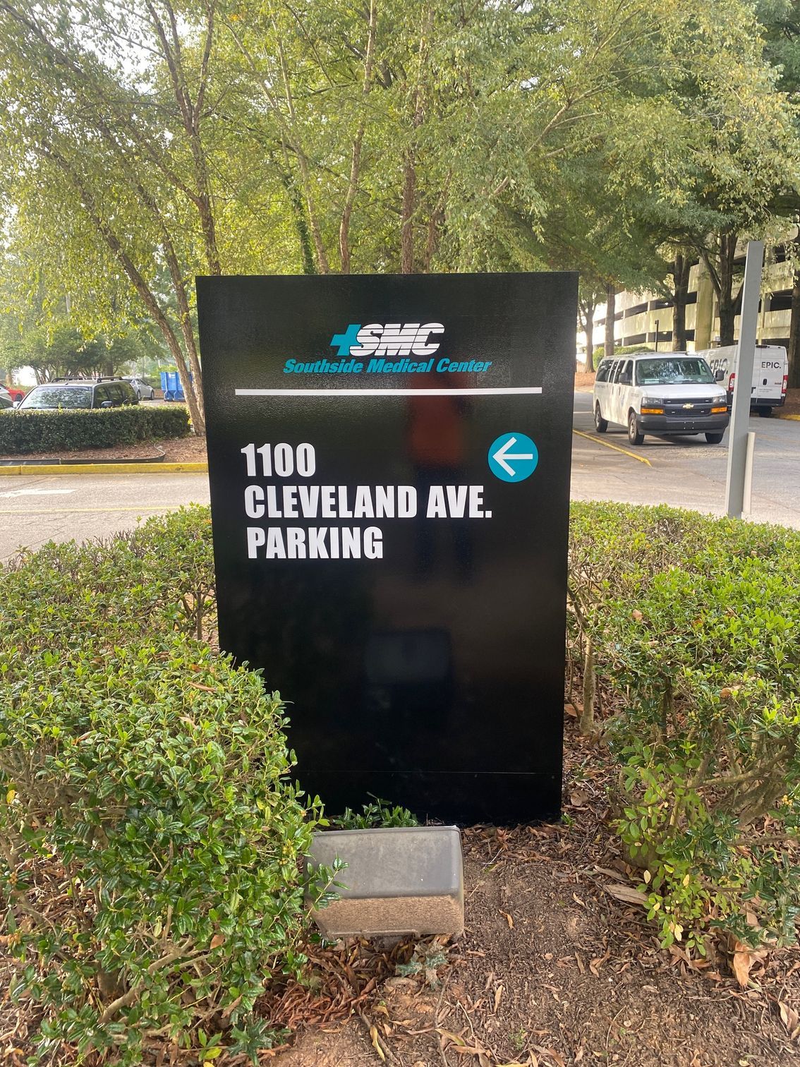 A black sign that says 1100 cleveland ave parking is in front of a parking lot.