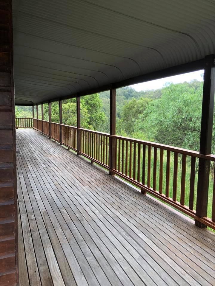 A Long Wooden Deck with A Railing and Trees in The Background — Alcando Renovations & Maintenance In Old Bar, NSW