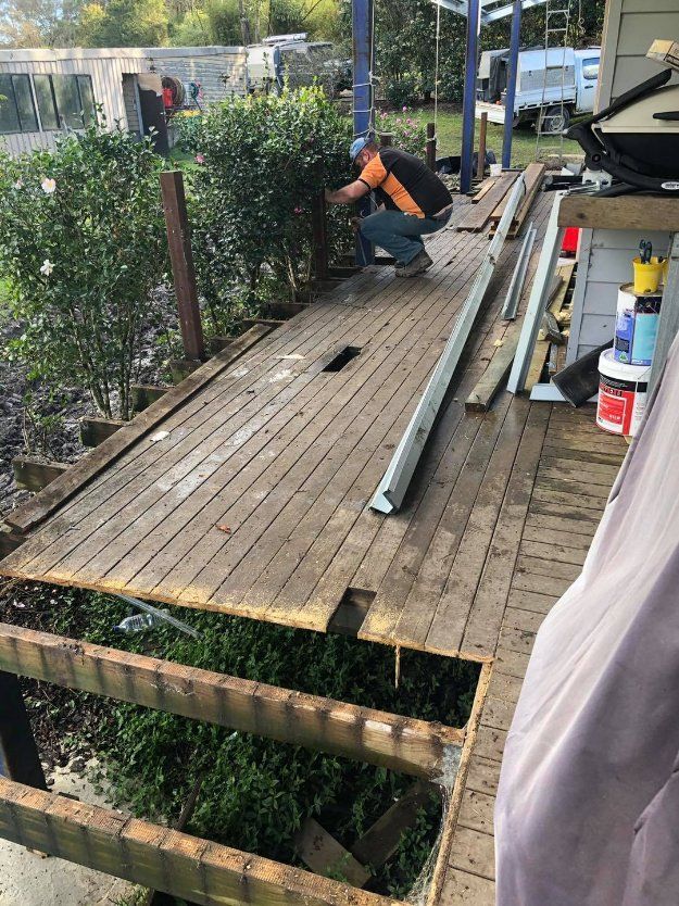 A Man Is Kneeling Down on A Wooden Deck — Alcando Renovations & Maintenance In Mid North Coast, NSW