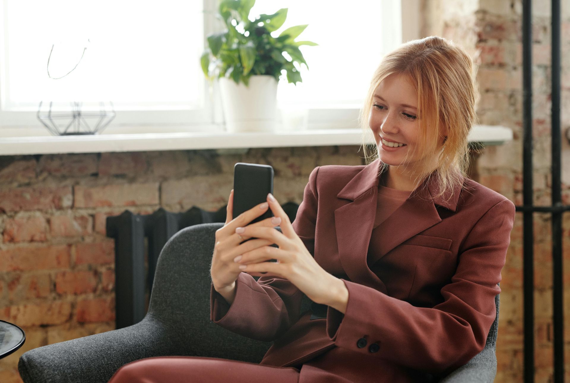 A woman in a suit is sitting in a chair looking at her cell phone.