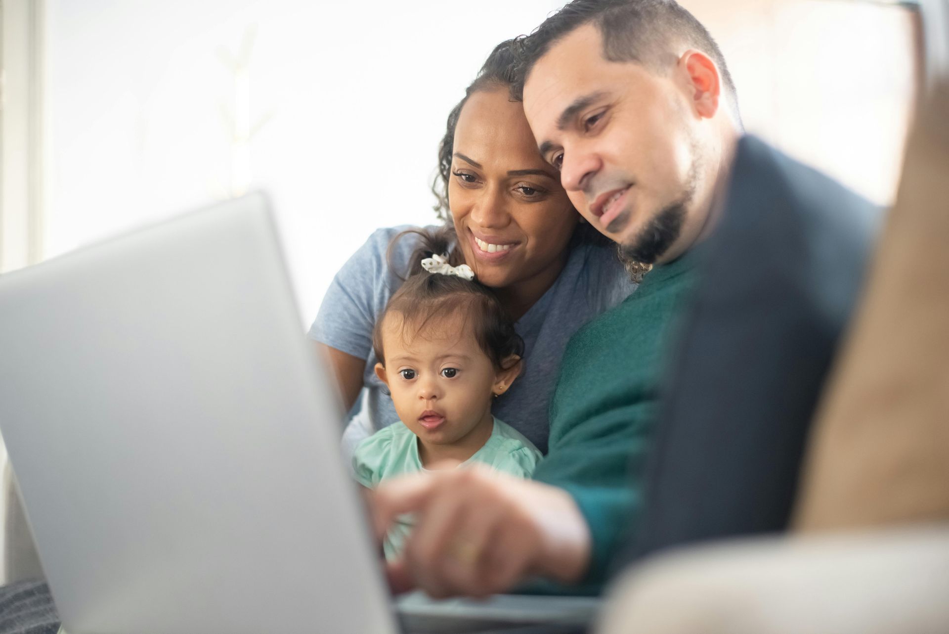 A family is sitting on a couch looking at a laptop computer.