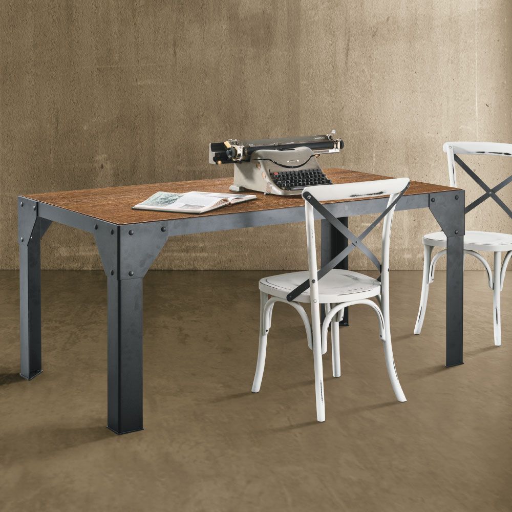 Tavolo in stile industriale con gambe in metallo e piano in legno, macchina da scrivere e due sedie bianche di fronte a una parete strutturata.