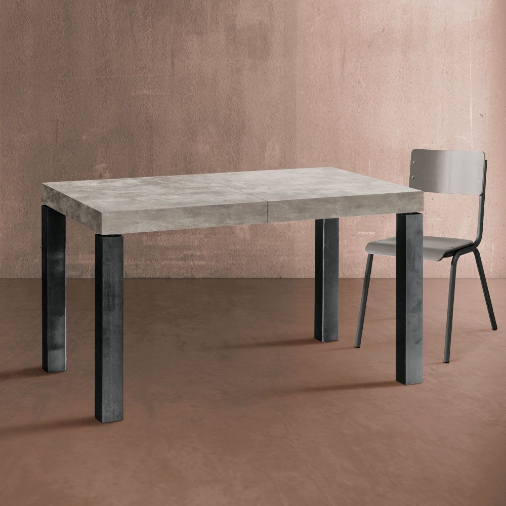 Tavolo in cemento con gambe in metallo scuro, una sedia grigia, contro una parete color pesca.