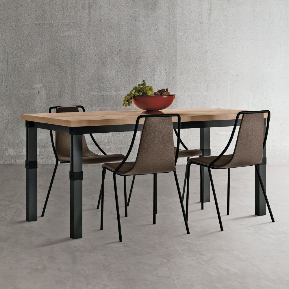 Tavolo da pranzo con piano in legno e gambe nere, quattro sedie, una ciotola di frutta, contro una parete grigia.