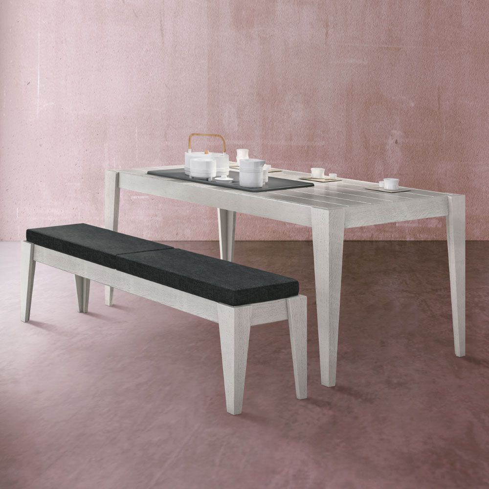 Tavolo da pranzo rettangolare bianco e panca con seduta imbottita nera contro una parete rosa.