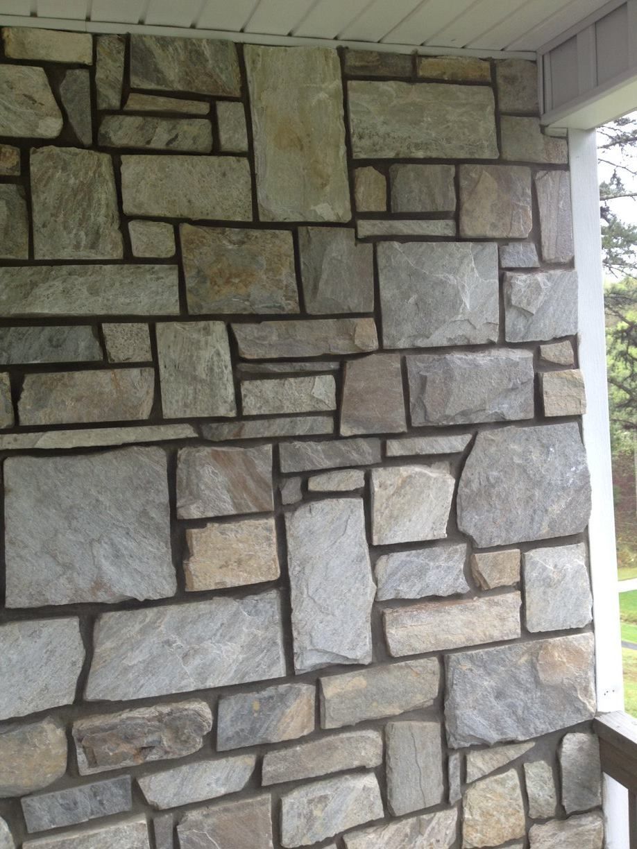 Stone wall with varied rectangular and square gray and tan stones, dark mortar.