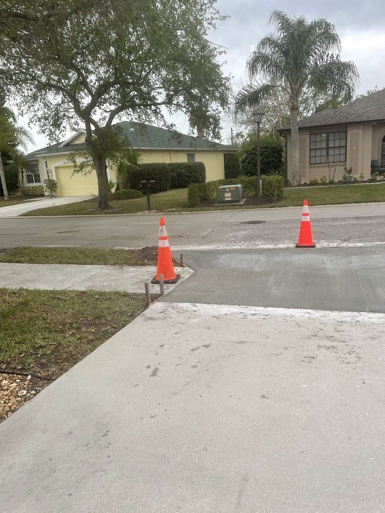 Two orange traffic cones are on the sidewalk in front of a house
