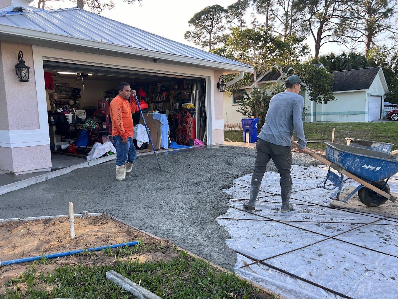 Two men are working on a driveway in front of a garage.