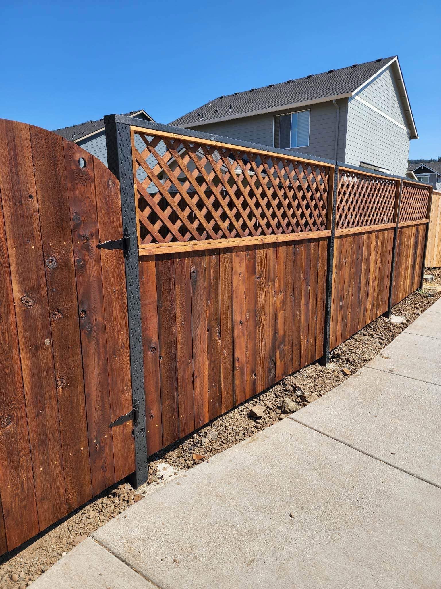 Wooden privacy fence with lattice top along a sidewalk beside a house under a clear sky