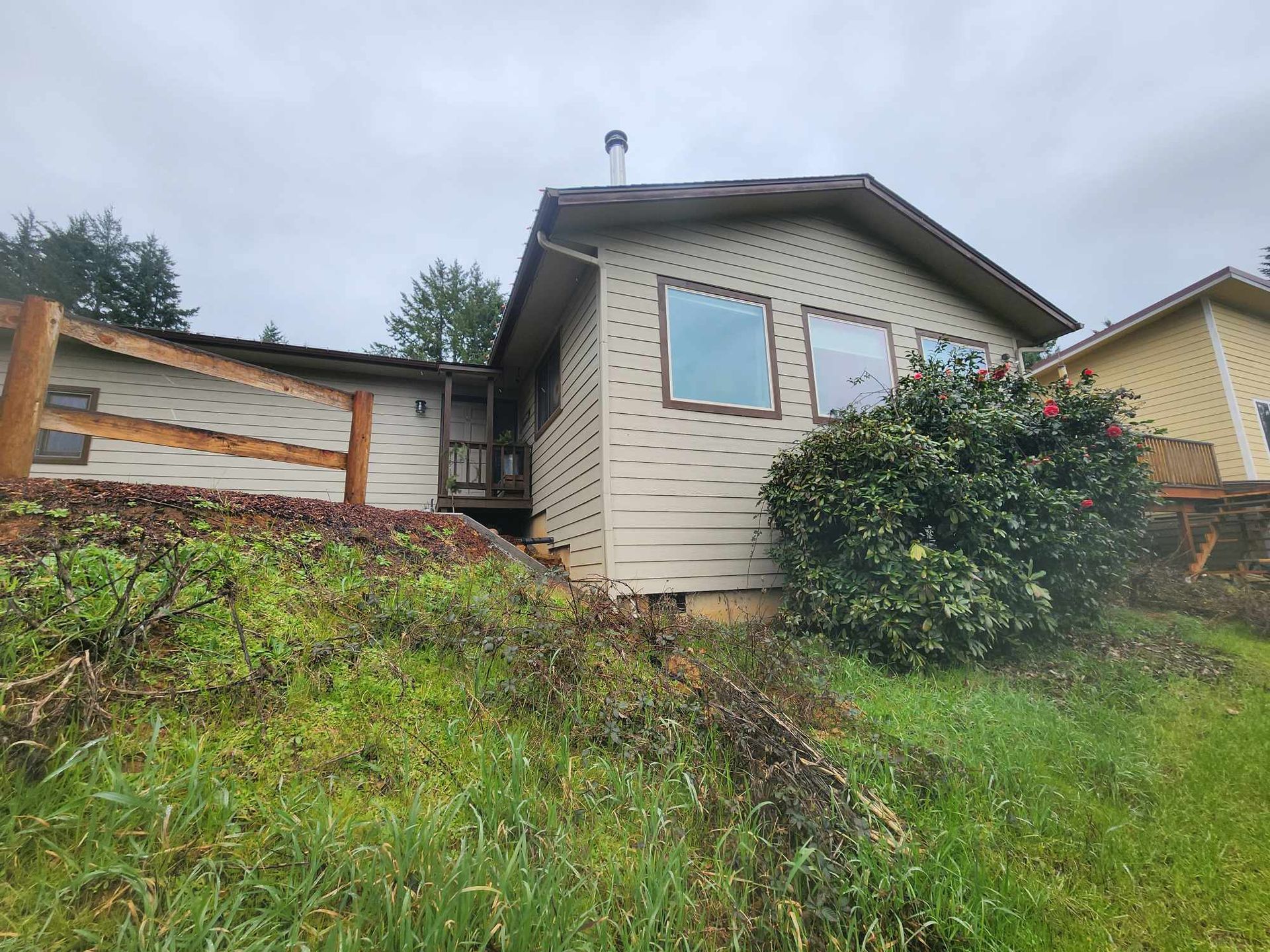 Small beige house on a grassy slope with bushes and a cloudy sky.