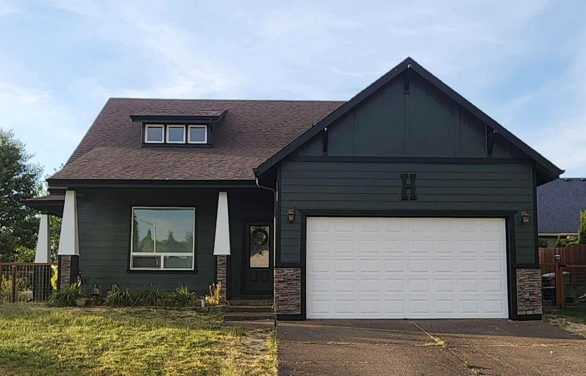 Suburban house with dark roof, white garage door, and front lawn under a blue sky
