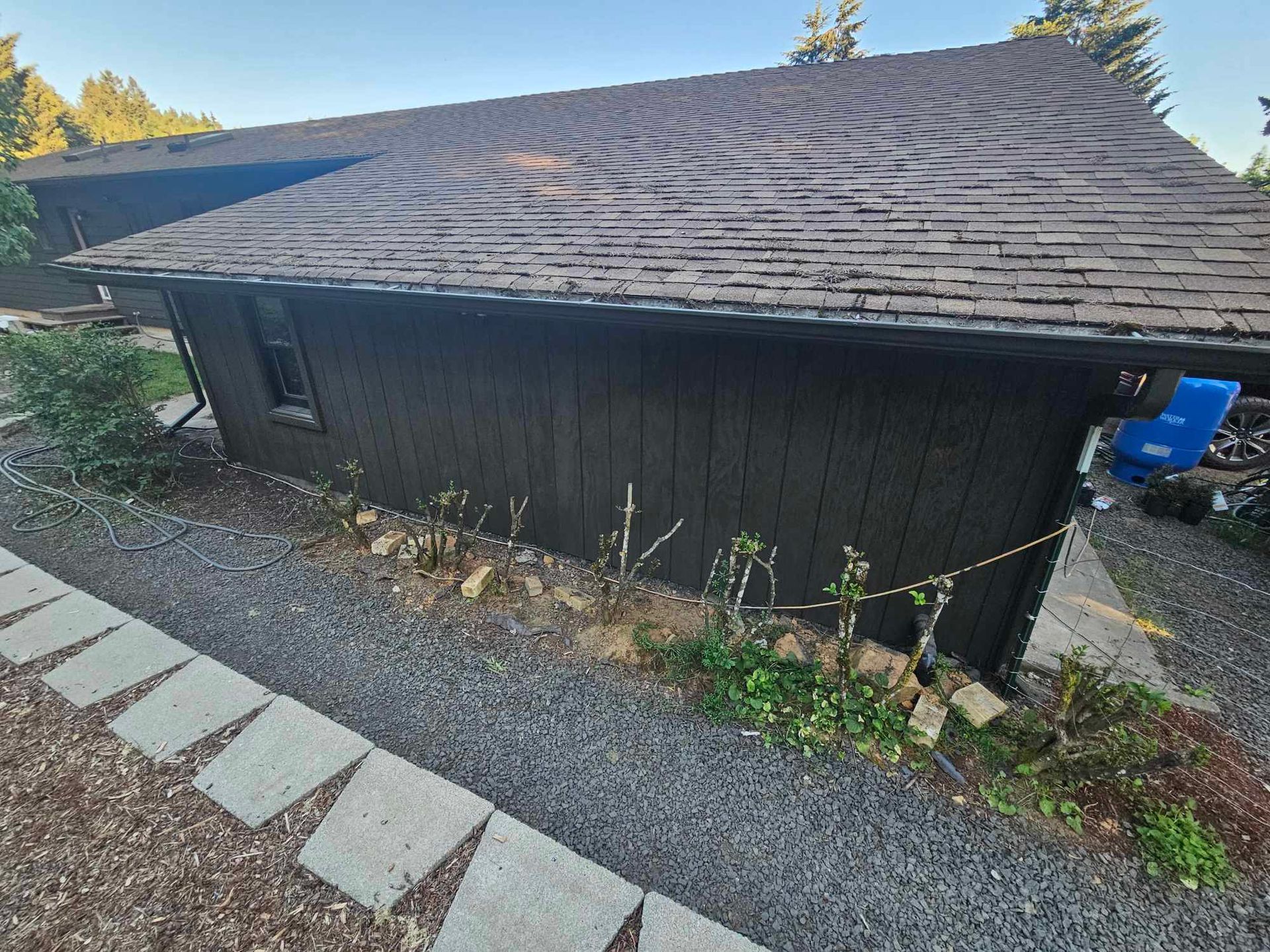 Dark house with shingled roof beside gravel yard and stepping-stone path outdoors